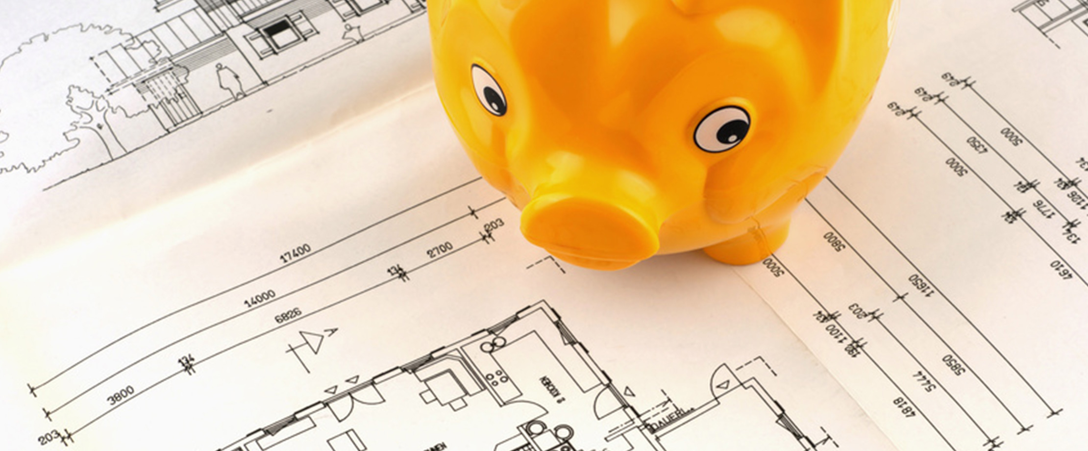 Ein oranges Sparschwein steht auf verschiedenen Plänen von Häusern und Bauprojekten